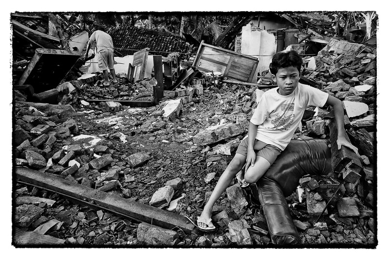 A Indonesian earthquake survivor sits outside his damaged home