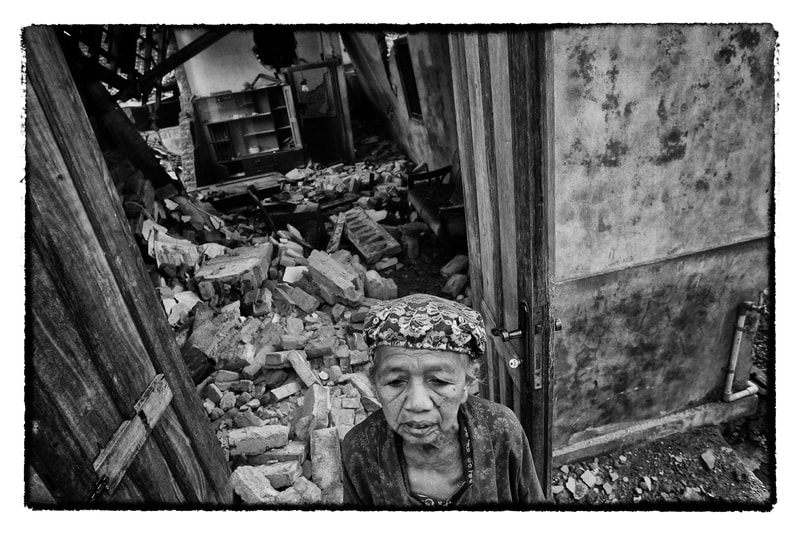Indonesian woman outside earthquake damaged home