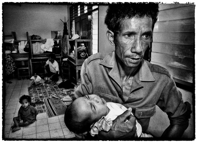 East Timor man hold child at refugee center